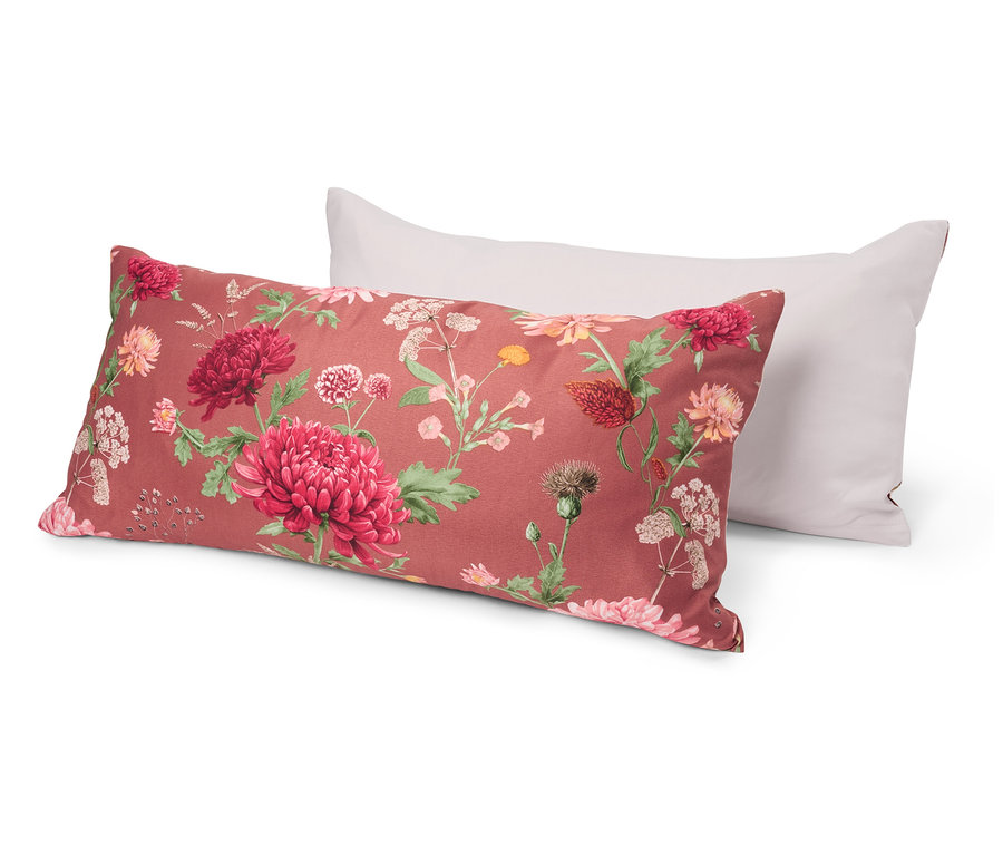 Dva polštáře leží na sobě. Spodní polštář má květinový vzor s červenými a růžovými květy na červeném pozadí. Horní polštář je bílý.