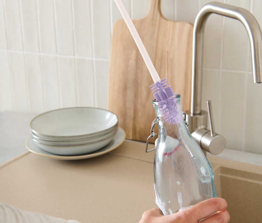 Ruka myje láhev pomocí štětky na láhve.
