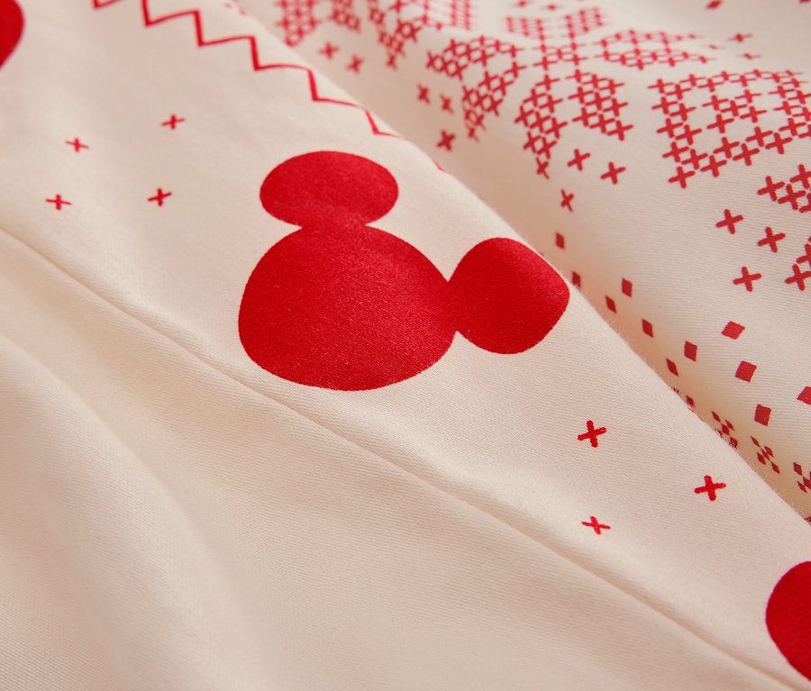 Detail bílého povlečení s červeným vzorem Mickey Mouse a vánočními motivy.