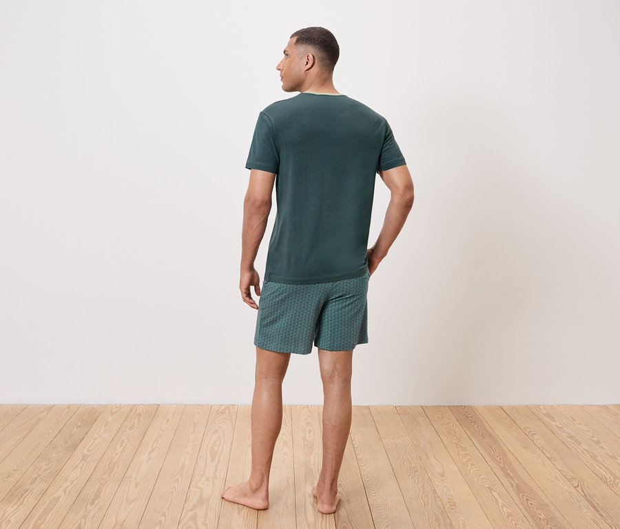 Muž zády k fotoaparátu má na sobě zelené tričko a vzorované šortky.