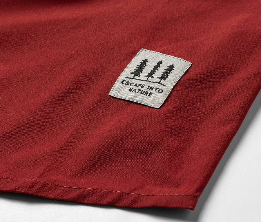 Detail červené outdoorové košile s nášivkou s motivem stromů a nápisem „ESCAPE INTO NATURE“.