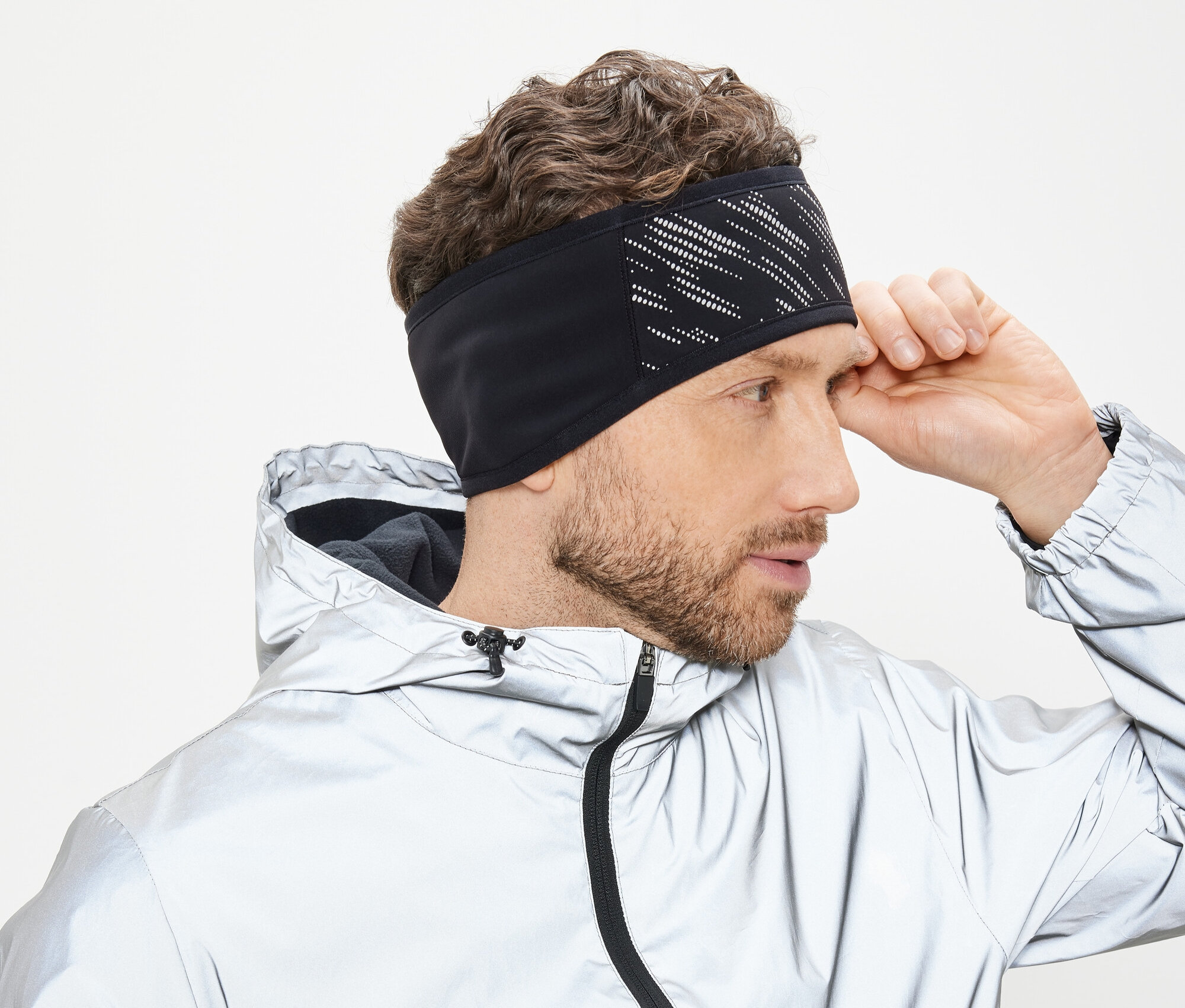 Muž si upravuje černou čelenku s bílým vzorem. Má na sobě stříbrnou bundu s kapucí.
