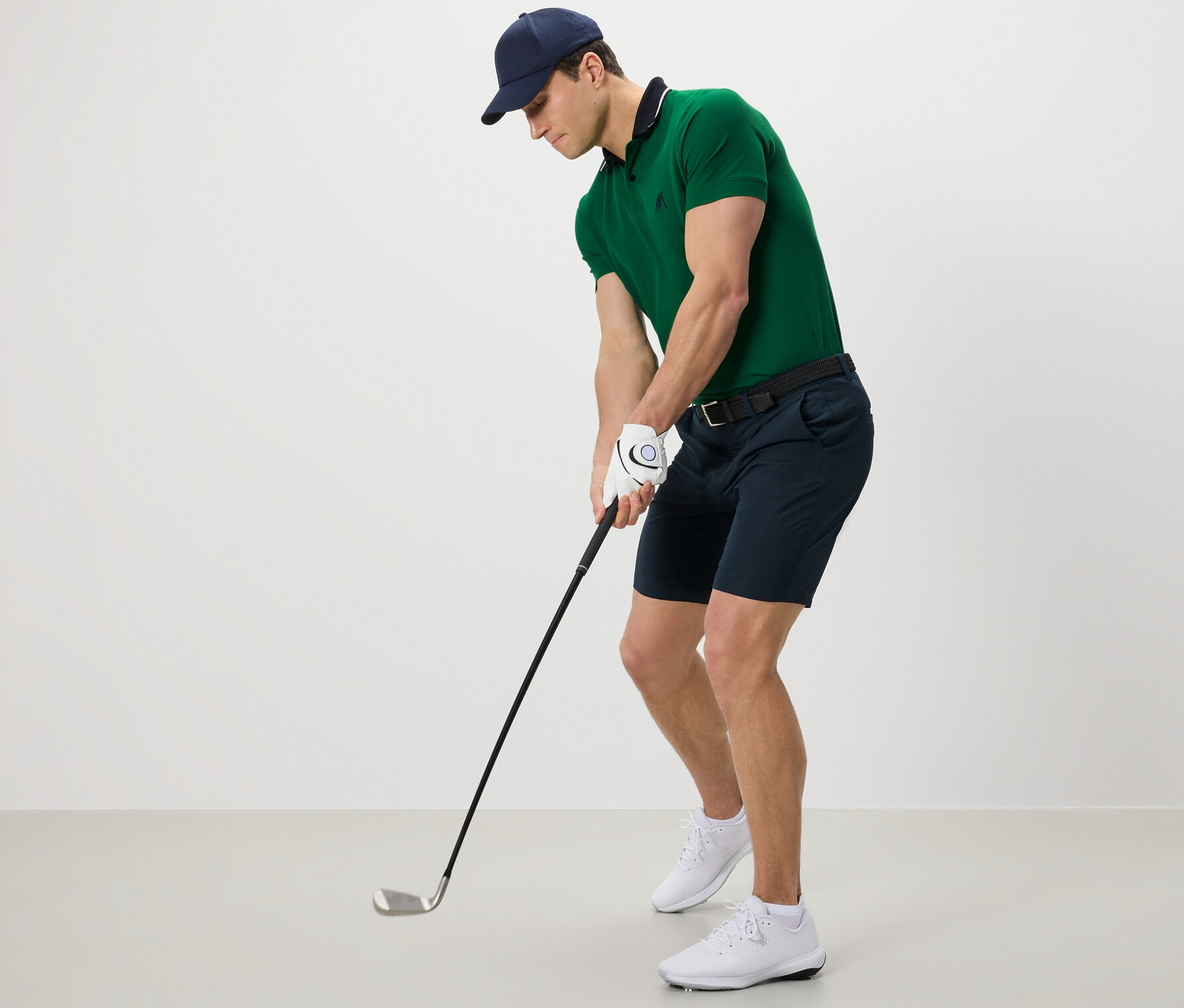 Muž v zelené polokošili a funkčních šortkách hraje golf.