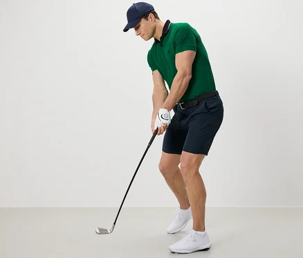 Muž v zelené polokošili a funkčních šortkách hraje golf.