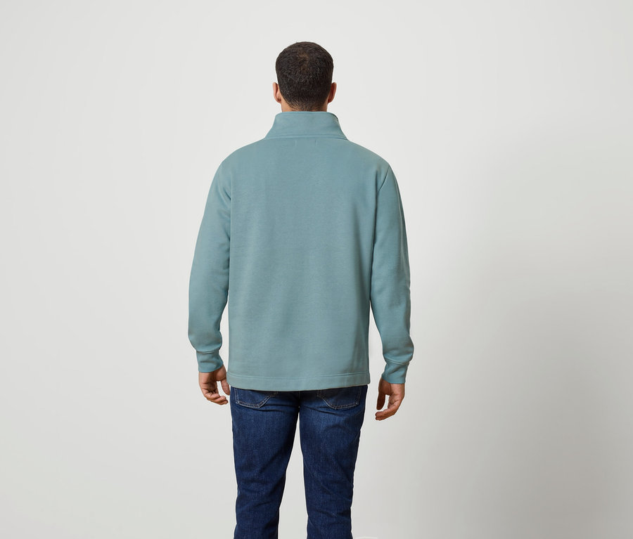 Muž zády k fotoaparátu má na sobě modrozelenou mikinu na zip a džíny.