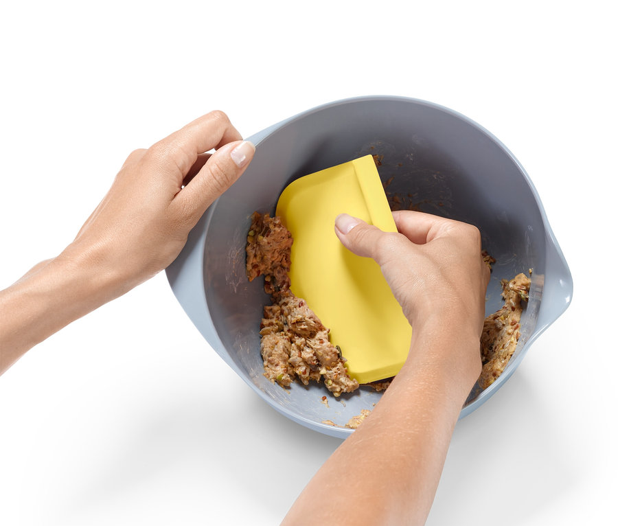 Pár rukou míchá těsto v míse žlutou stěrkou.