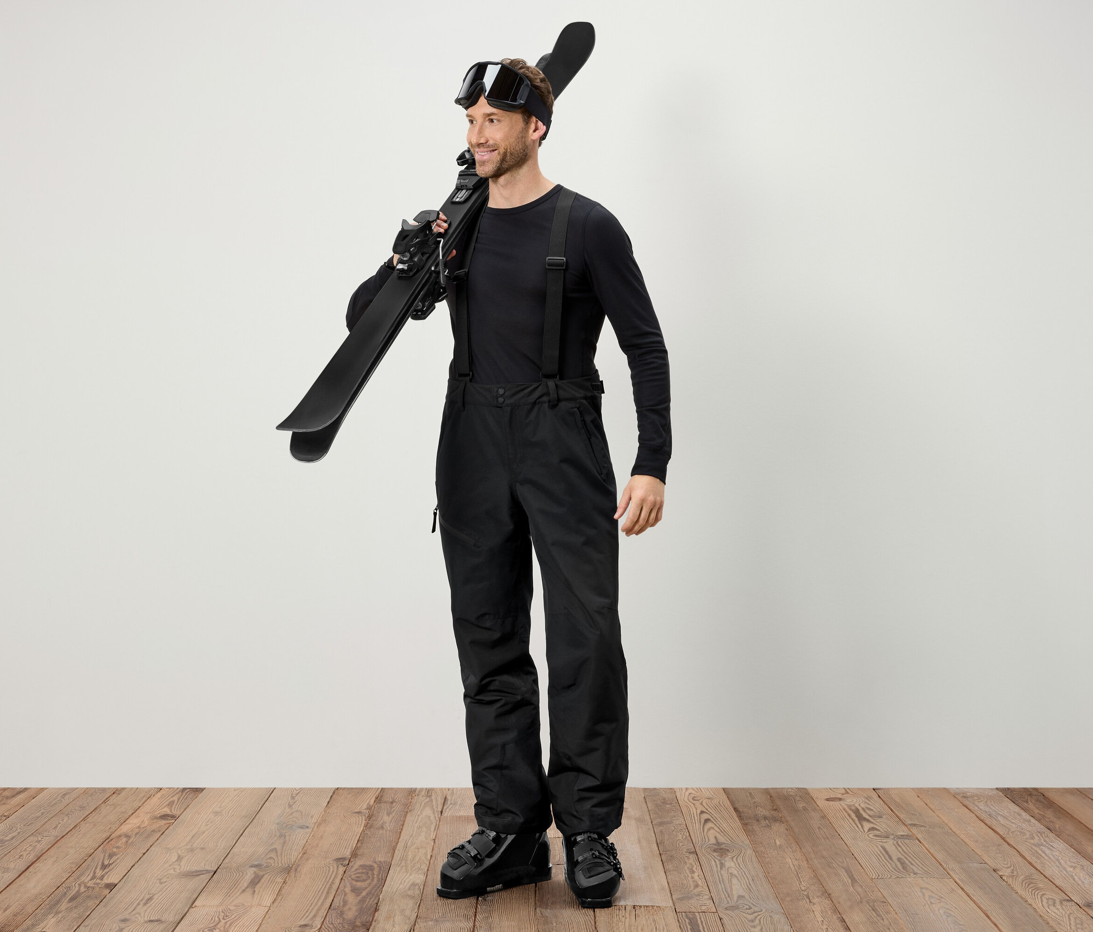 Muž v černém lyžařském oblečení nese lyže přes rameno.