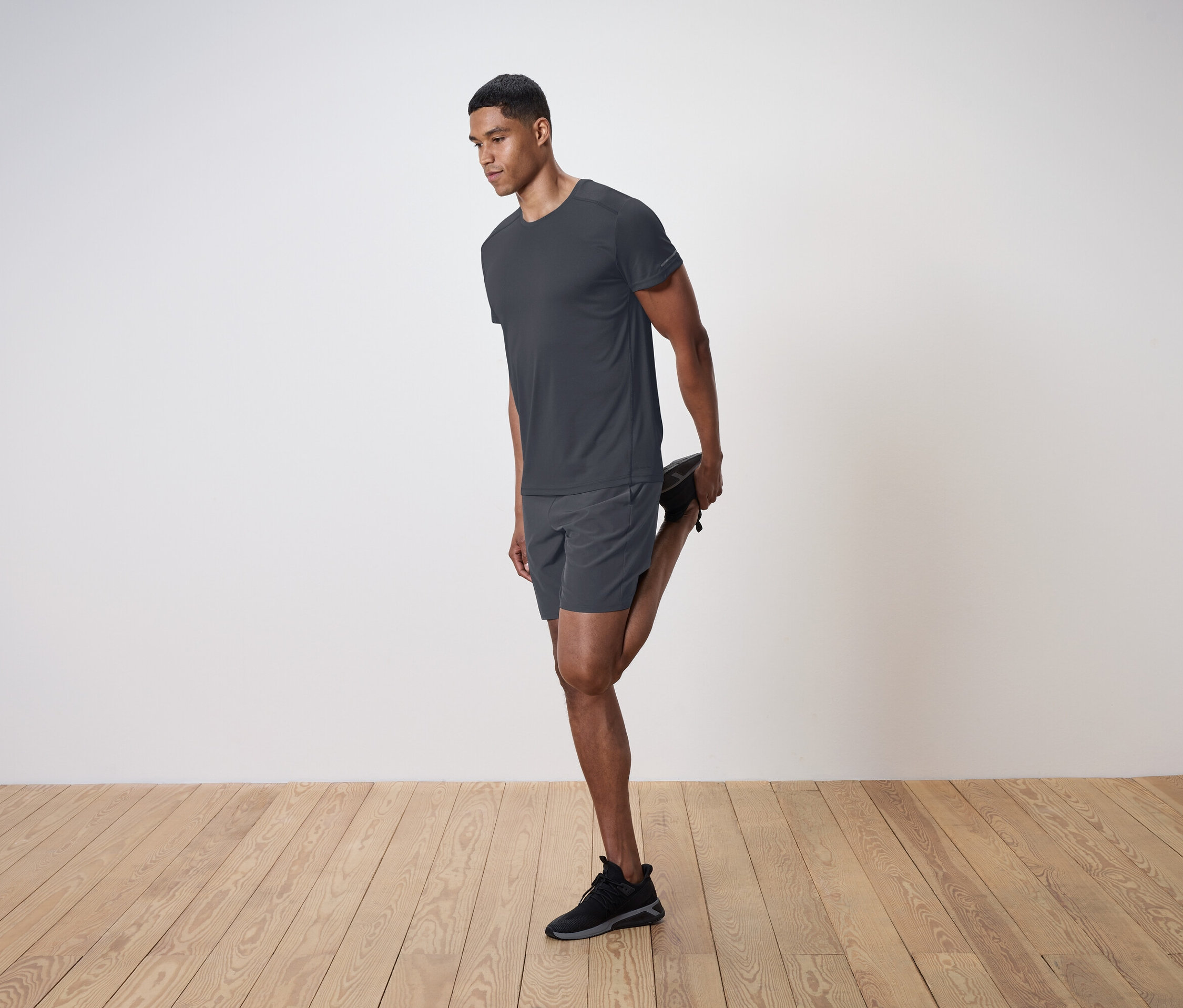 Muž protahuje kvadriceps na pozadí bílé stěny.