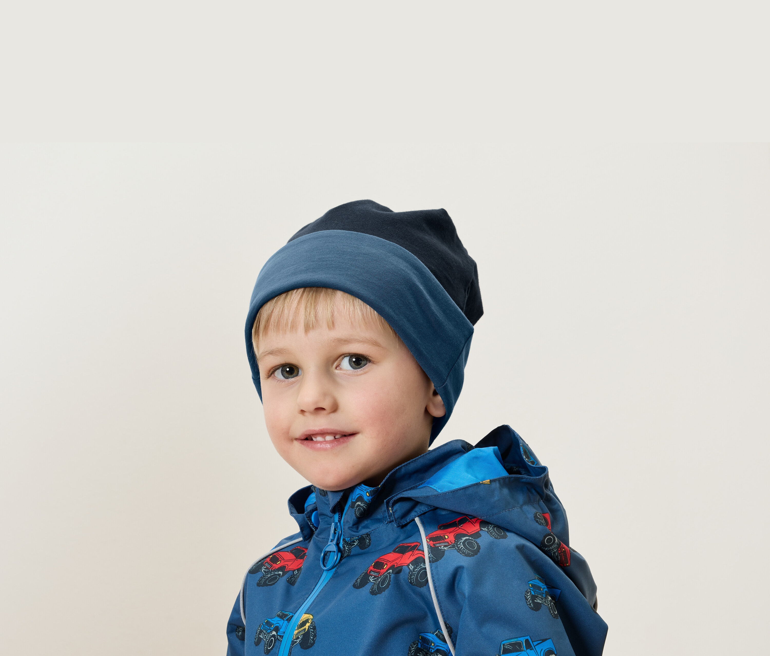 Portrét chlapce s blond vlasy v modré čepici a bundě s potiskem aut.