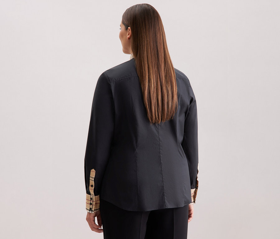 Pohled zezadu na ženu s dlouhými hnědými vlasy v černé popelínové halence Seidensticker s kostkovaným detailem.