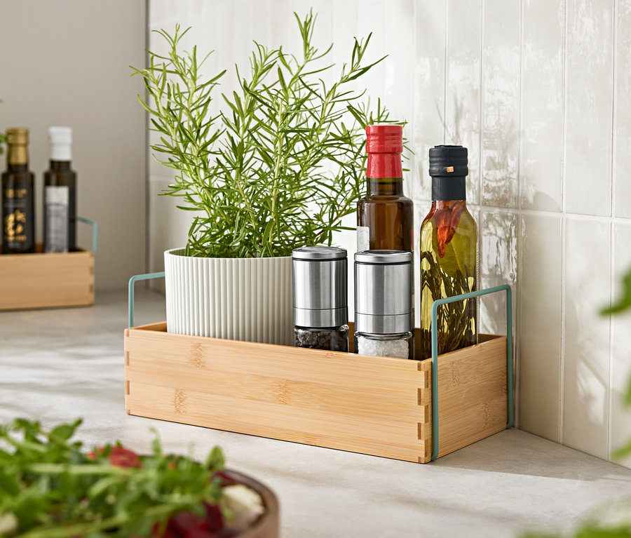 Bylinky v květináči, dva mlýnky na koření a dvě lahve oleje v dřevěném podnosu.