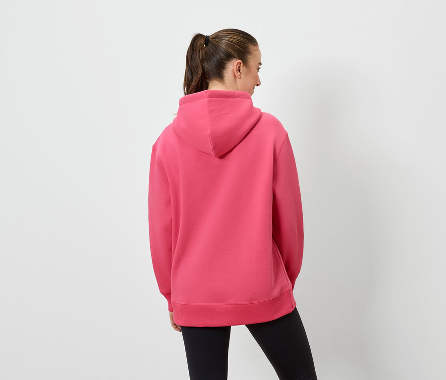 Žena zády k fotoaparátu má na sobě růžovou mikinu s kapucí a černé legíny.