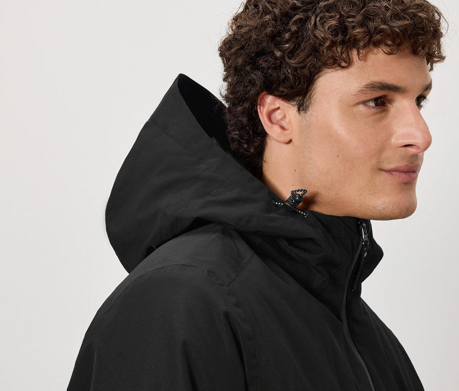 Muž s hnědými kudrnatými vlasy má na sobě černou bundu s kapucí.