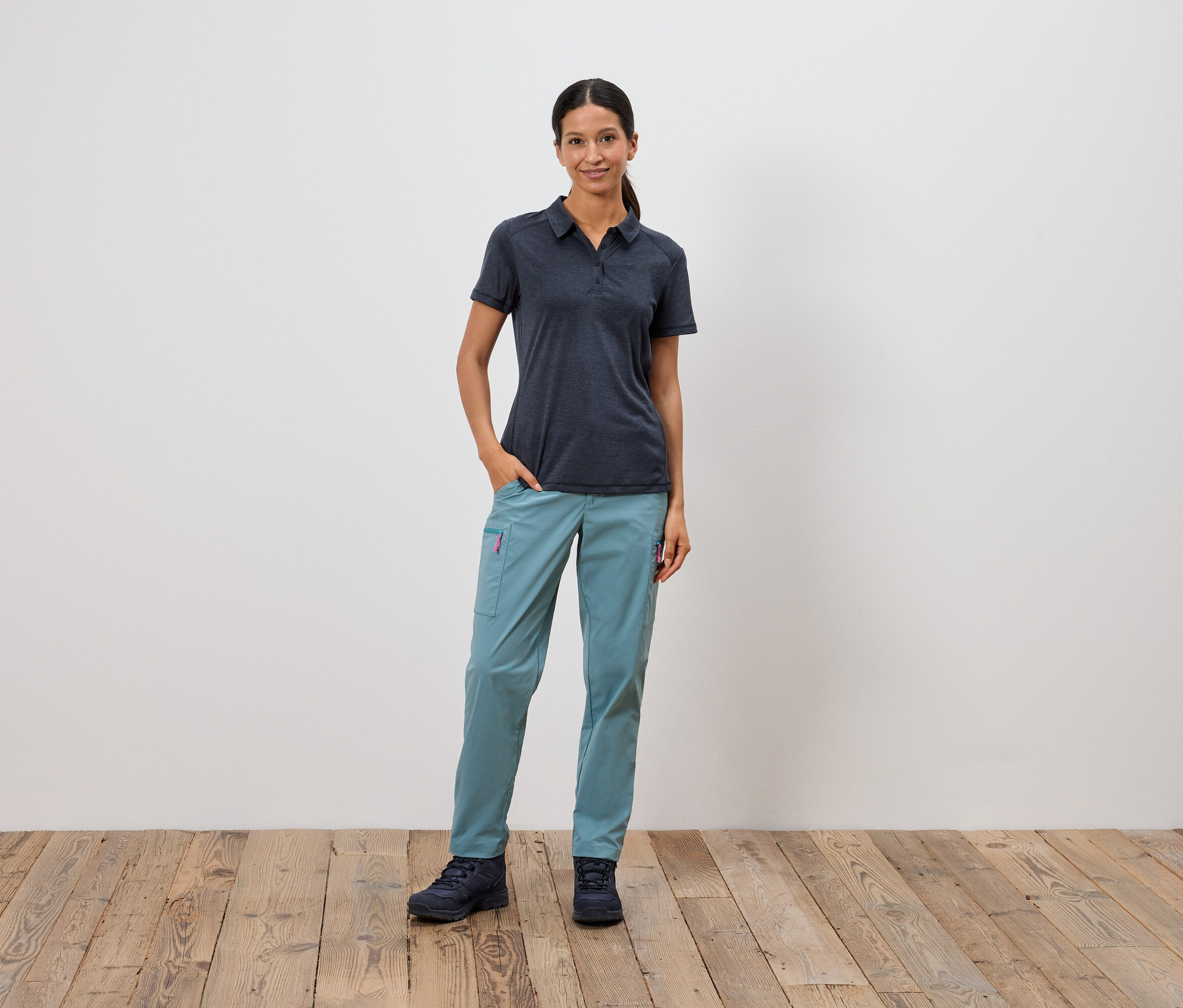 Žena stojí s rukou v kapse před bílou zdí.