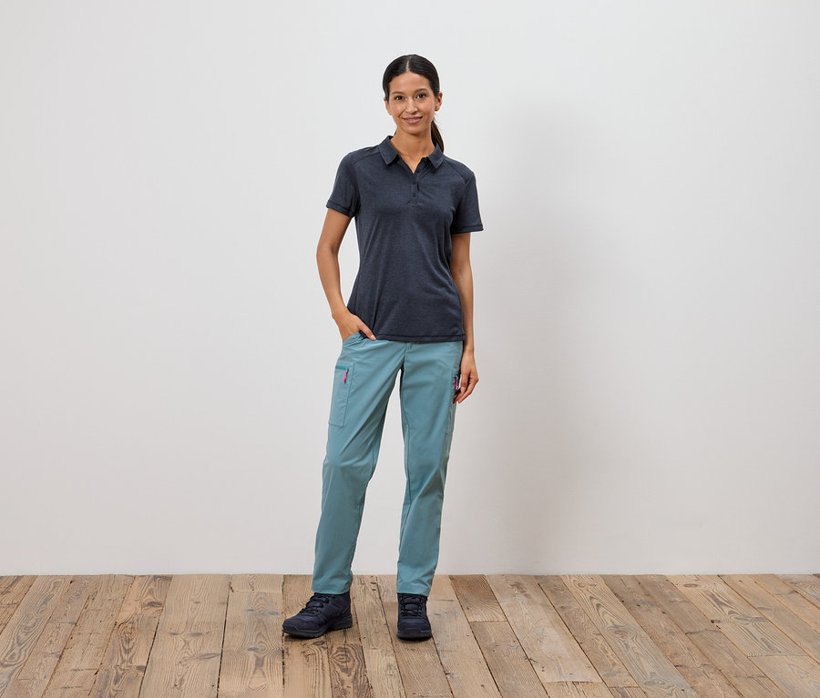 Žena stojí s rukou v kapse před bílou zdí.