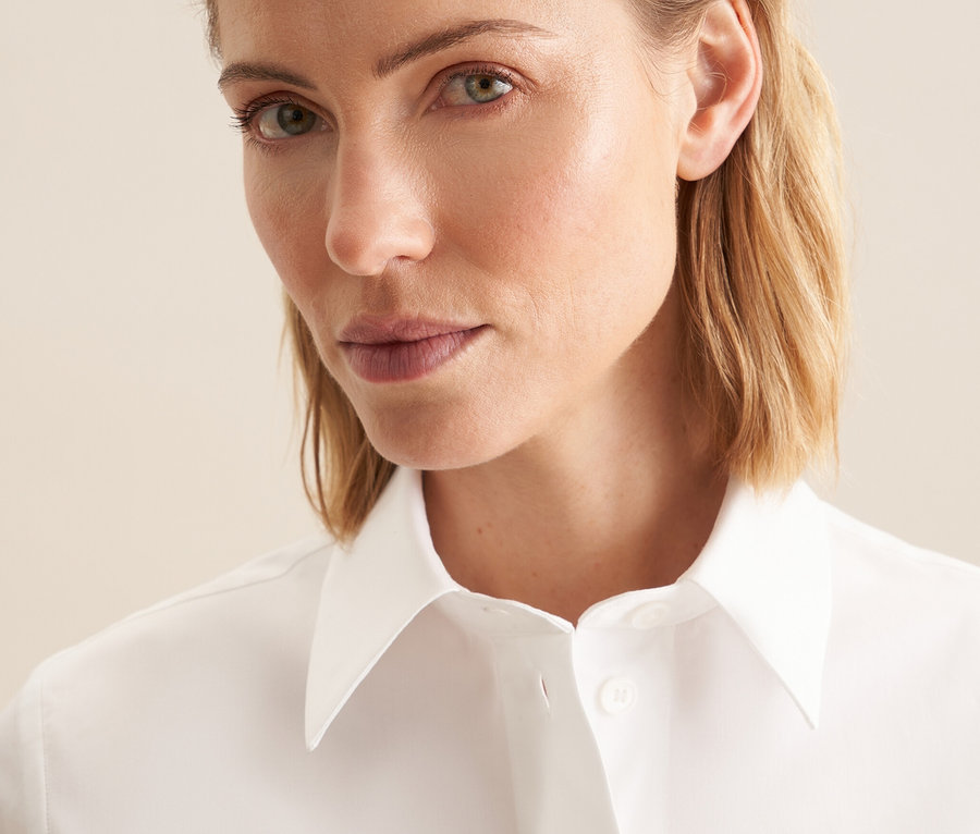 Portrét ženy s blond vlasy v bílé halence s krátkým rukávem Seidensticker.