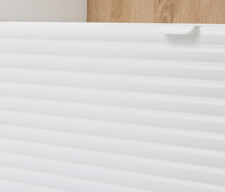 Detailní pohled na bílou skříňku s horizontálními drážkami a světle hnědým dřevěným prvkem v pozadí.