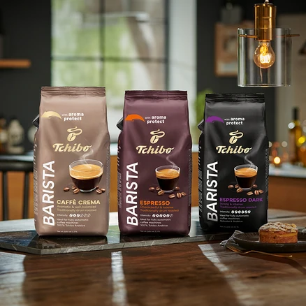 Tři balení zrnkové kávy Tchibo Barista stojí na stole, zleva doprava: Caffè Crema, Espresso a Espresso Dark.