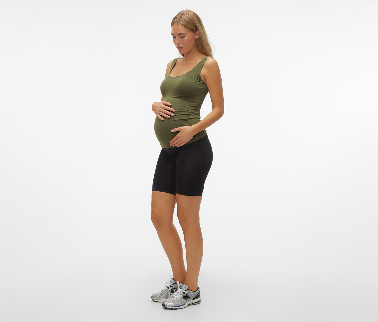 Těhotná žena v olivovém topu a skinny šortkách MAMALICIOUS »MLTIA JEANNE«, mellow buff, stojí bokem.