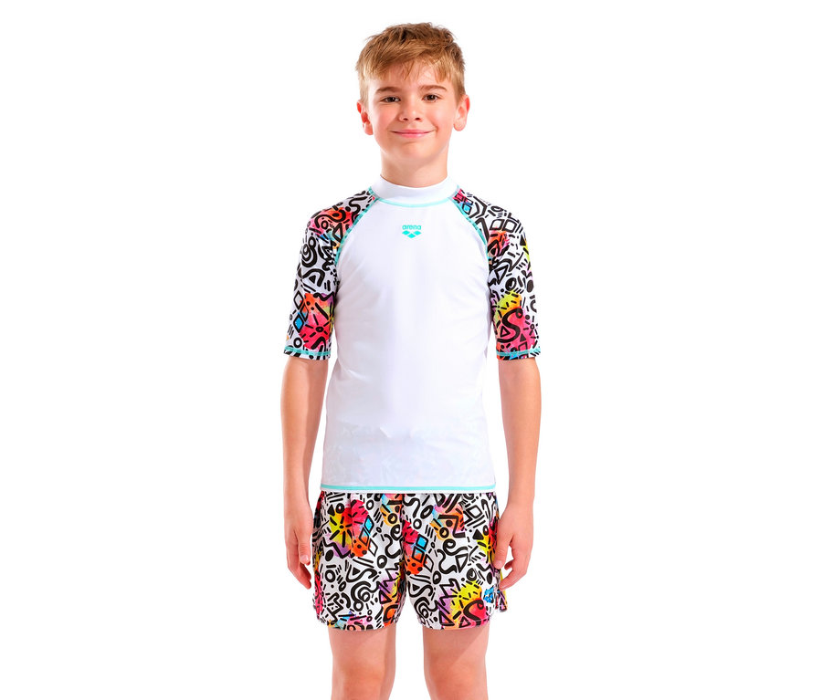Chlapec s blond vlasy má na sobě bílý top Arena s barevnými rukávy a odpovídající šortky.