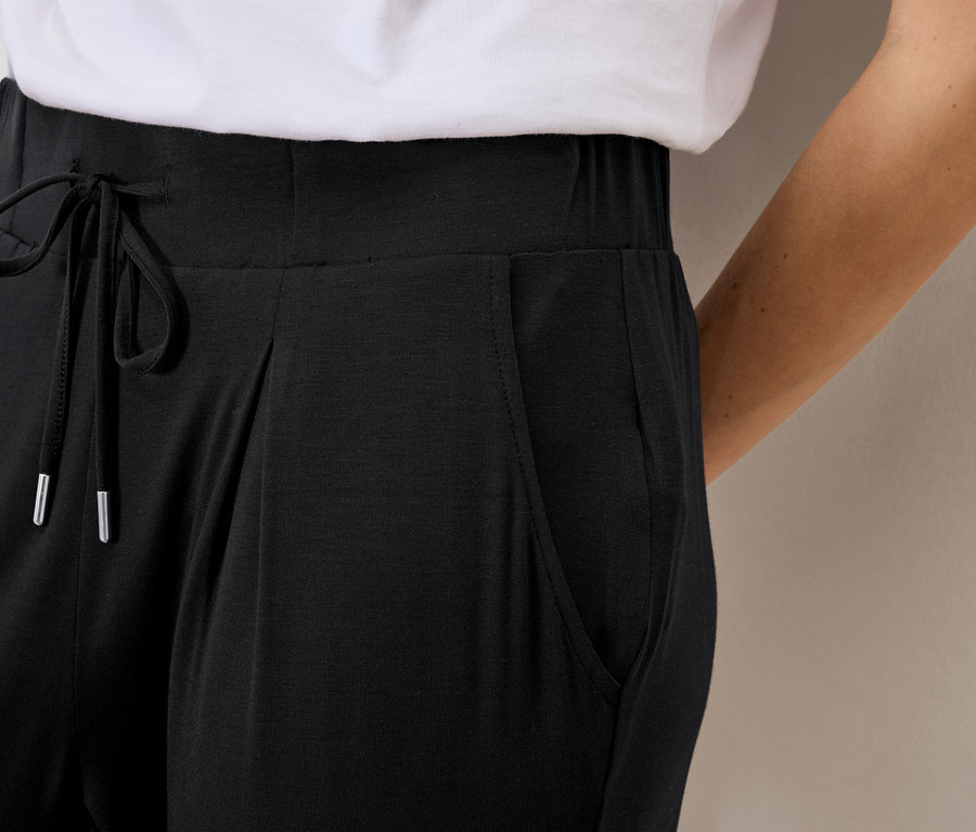 Detailní záběr ženy v černých volných kalhotách se stahovací šňůrkou a kapsami.