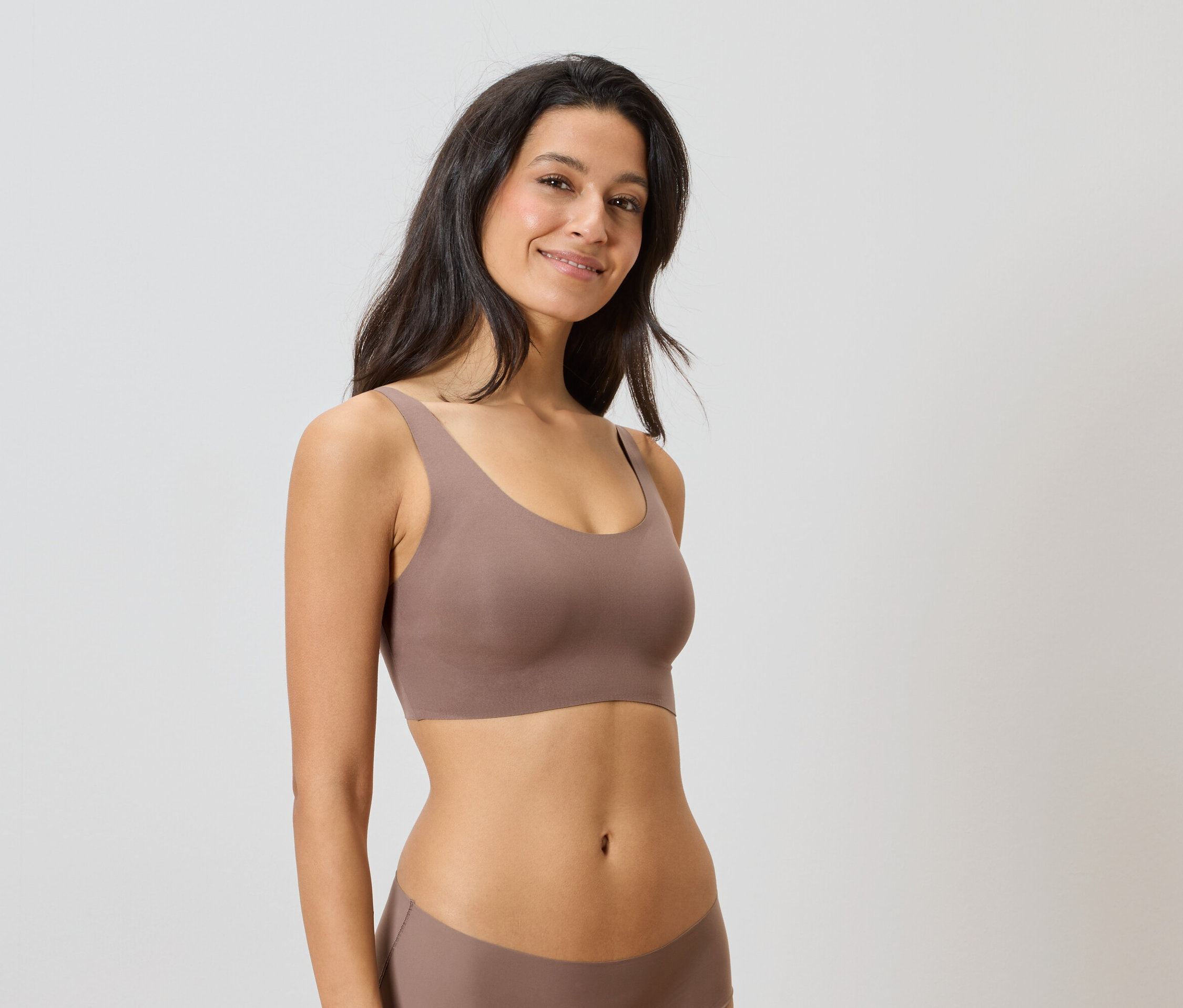 Žena má na sobě hnědou soupravu spodního prádla na neutrálním pozadí.