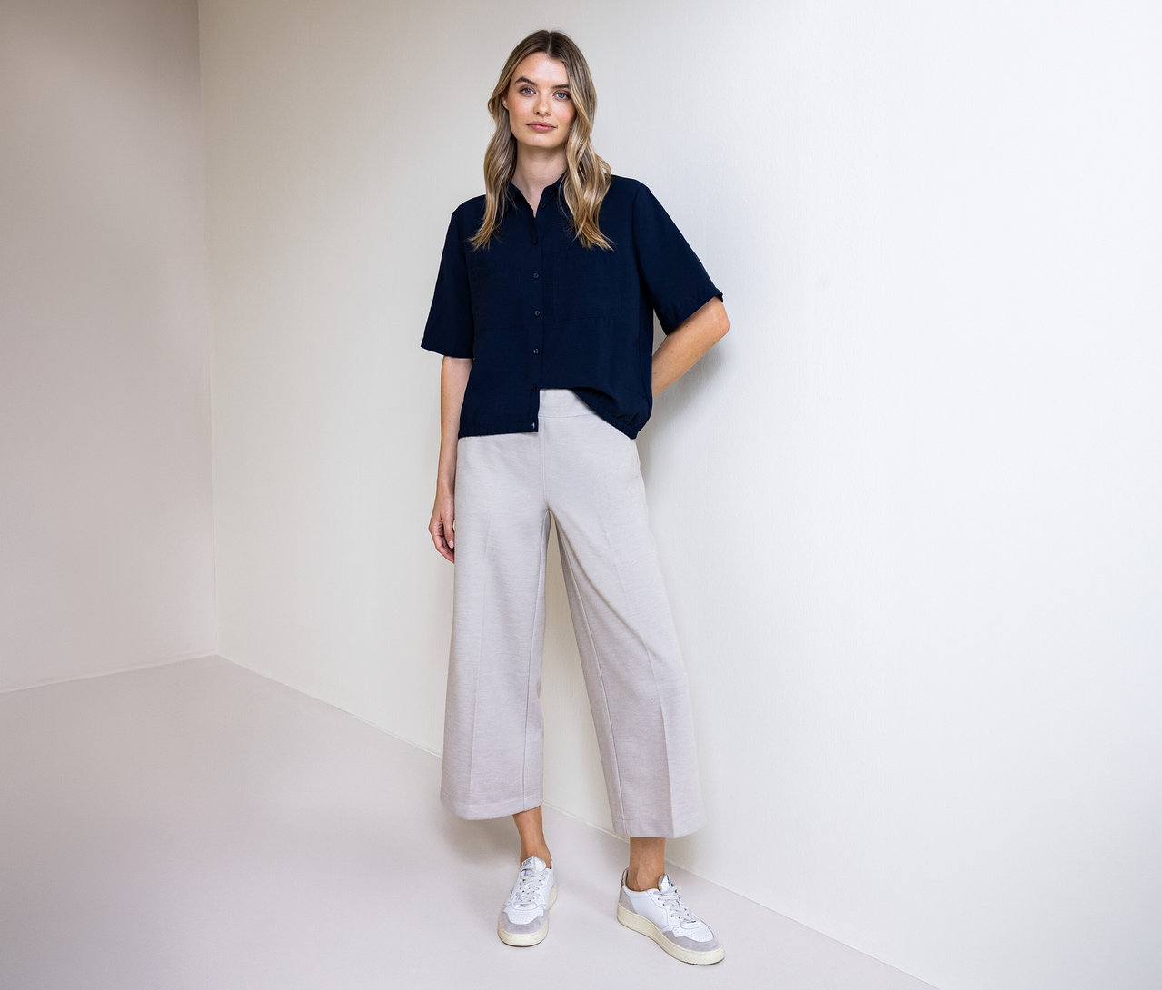 Žena v kalhotách a košilové halence Street One. Stojí před zdí.