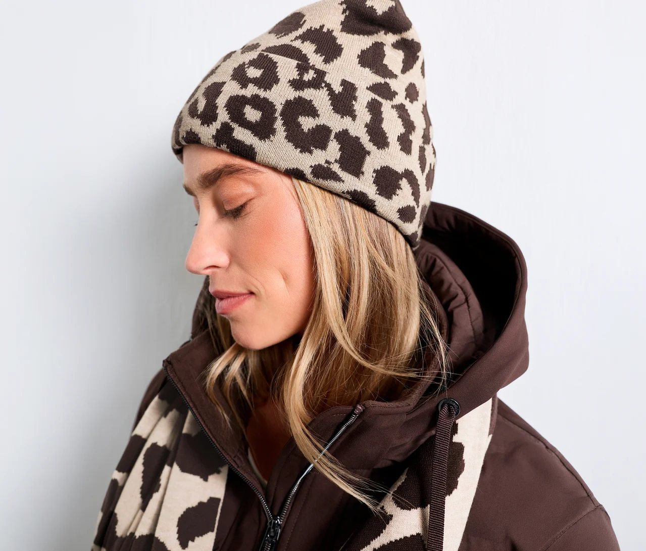 Žena má na sobě pletenou čepici Street One s hnědým leopardím vzorem, hnědou bundu a ladící šálu.