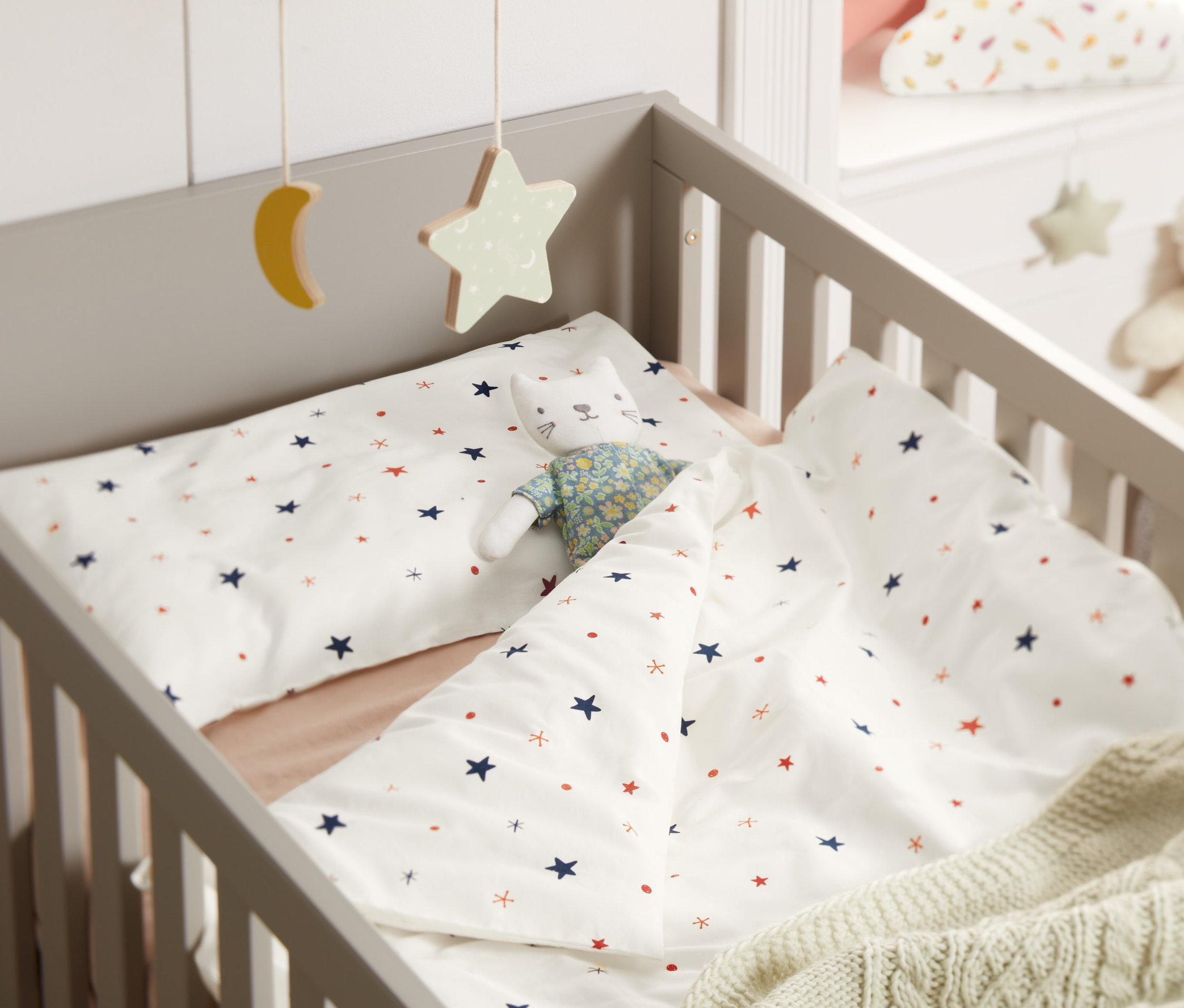 V postýlce je povlečení pro miminka s hvězdami a hračka kočky.