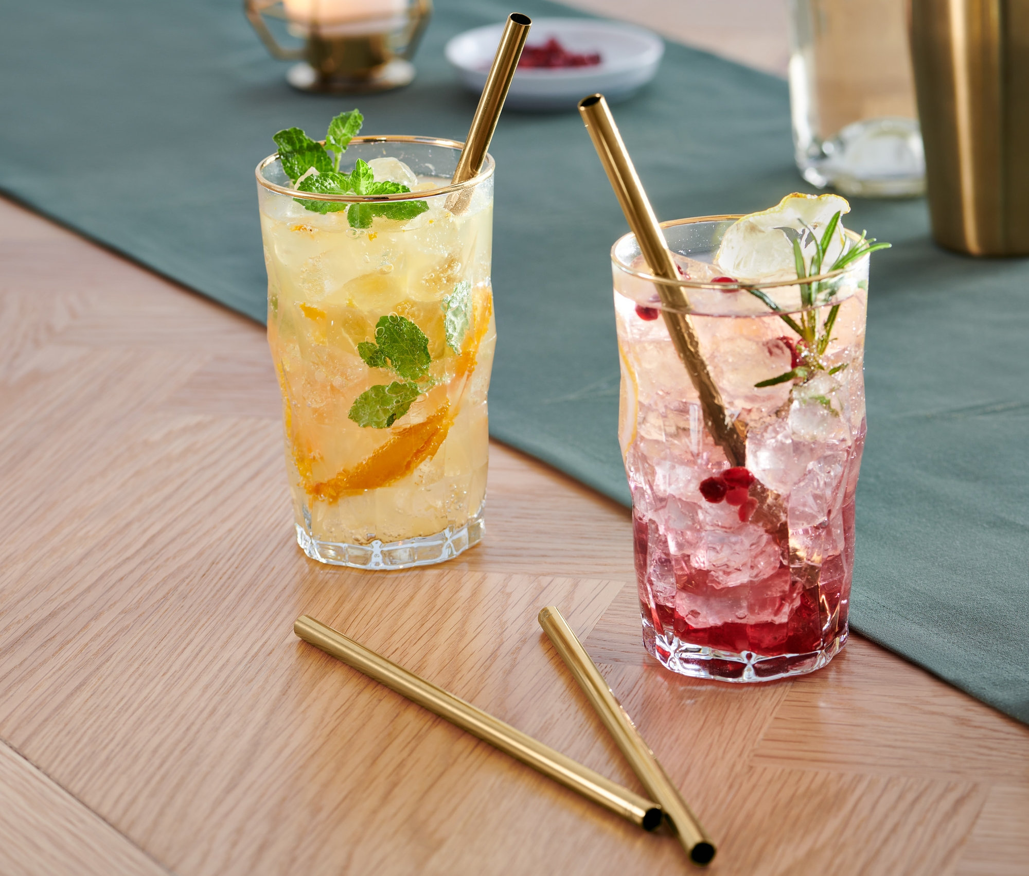 Dva nápoje s ledem a ovocem ve sklenicích se zlatými kovovými brčky, 4 ks jsou na stole.