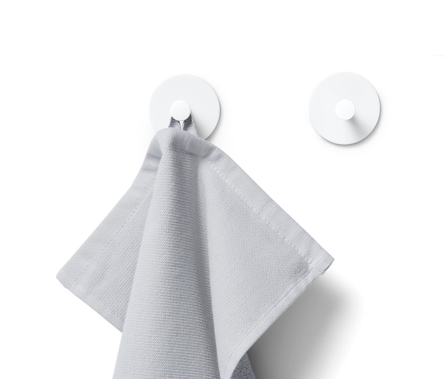 Šedý ručník visí na bílém háčku, v pozadí je vidět další bílý háček.
