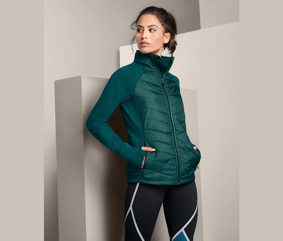 Žena pózuje v zelené běžecké termobundě s uschovatelnou kapucí.
