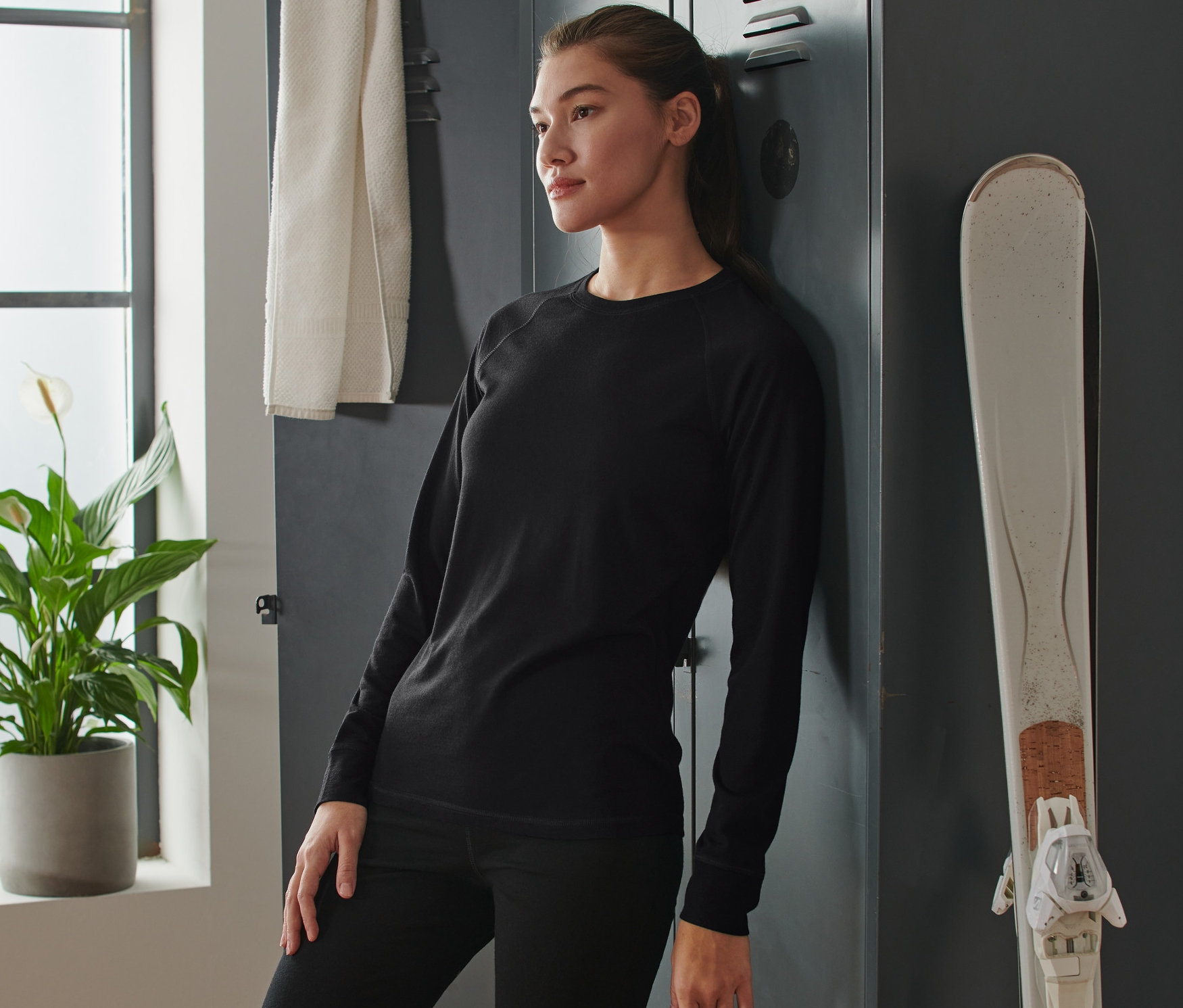 Žena se opírá o skříňku v černém funkčním triku s merino vlnou.