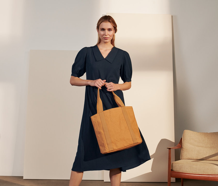 Žena drží v ruce shopper a má na sobě krepové halenkové šaty.
