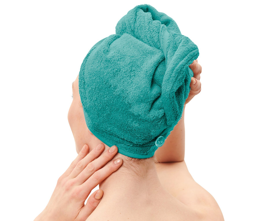 Žena si upravuje na hlavě modrozelený ručníkový turban.