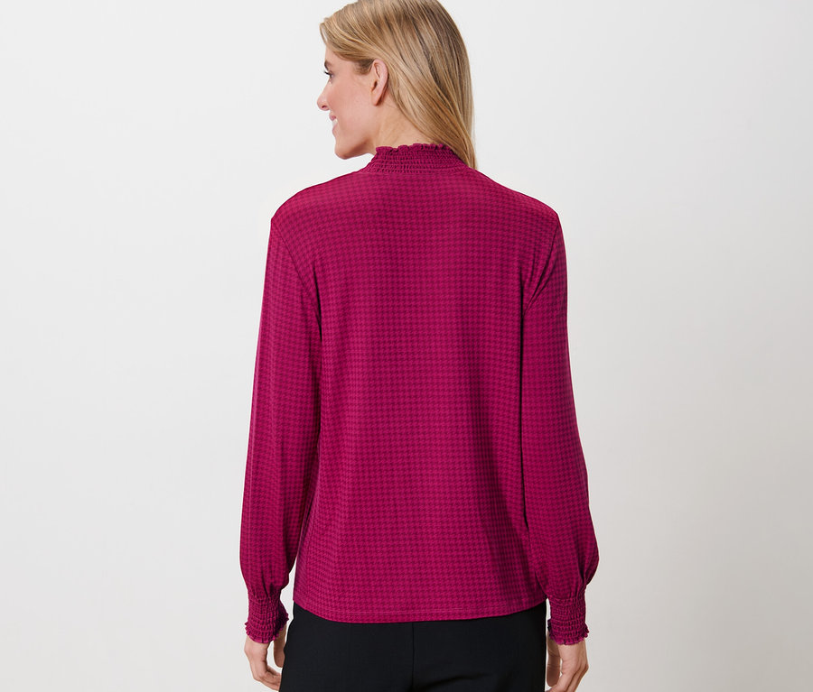 Žena má na sobě halenkové triko se stojáčkem a potiskem.