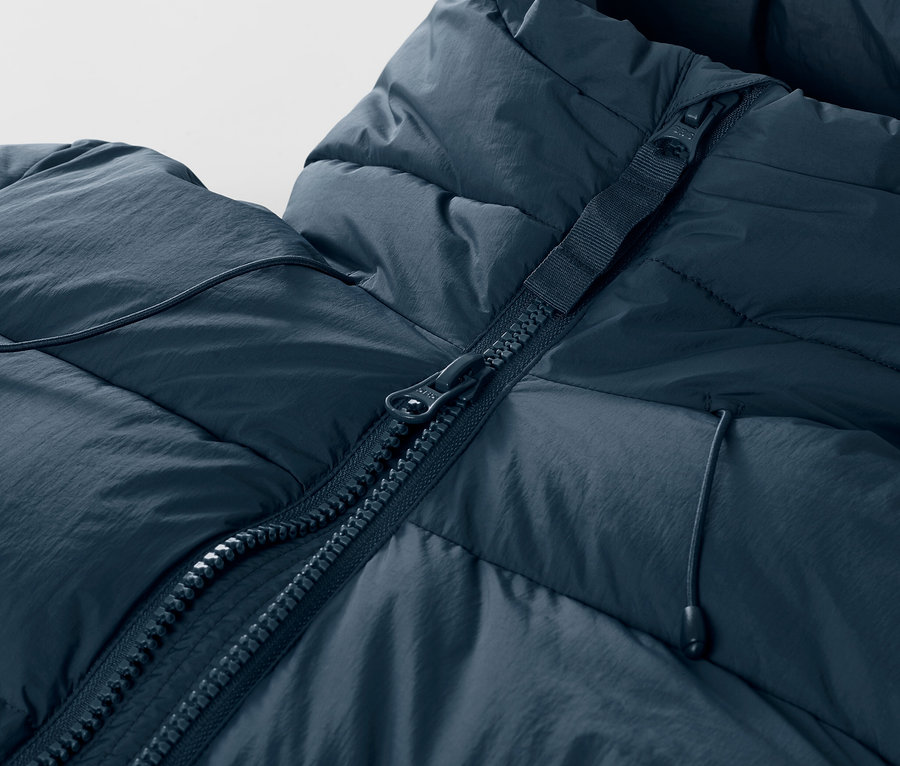 Detail tmavě modré prošívané lyžařské bundy se zipem.