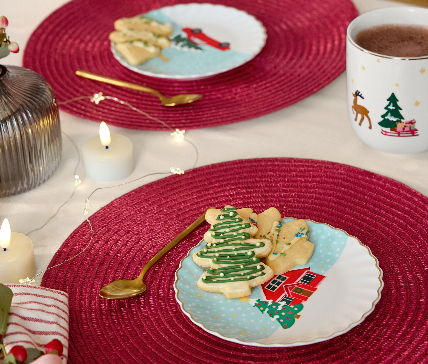 Dva stoly s červenými prostíráními, na nichž jsou dezertní talíře se zlatým dekorem, vykrajované cukroví a zlaté lžičky.