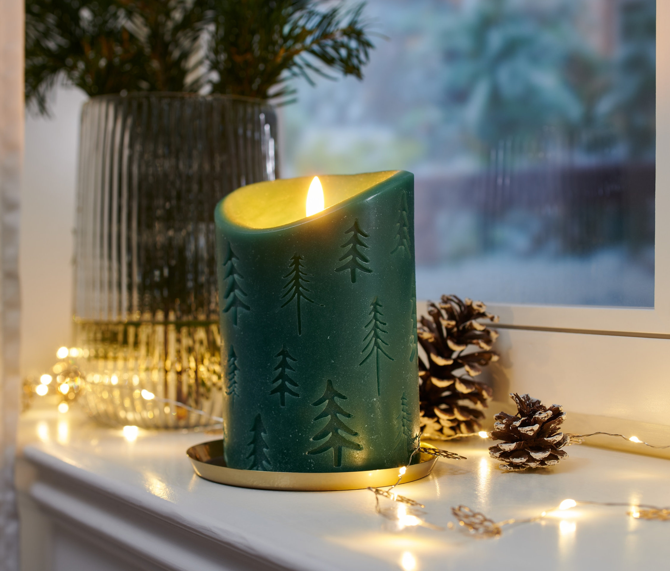 Zelená LED svíčka z pravého vosku se vzorem vánočního stromku na zlatém podnosu s šiškami a světýlky.