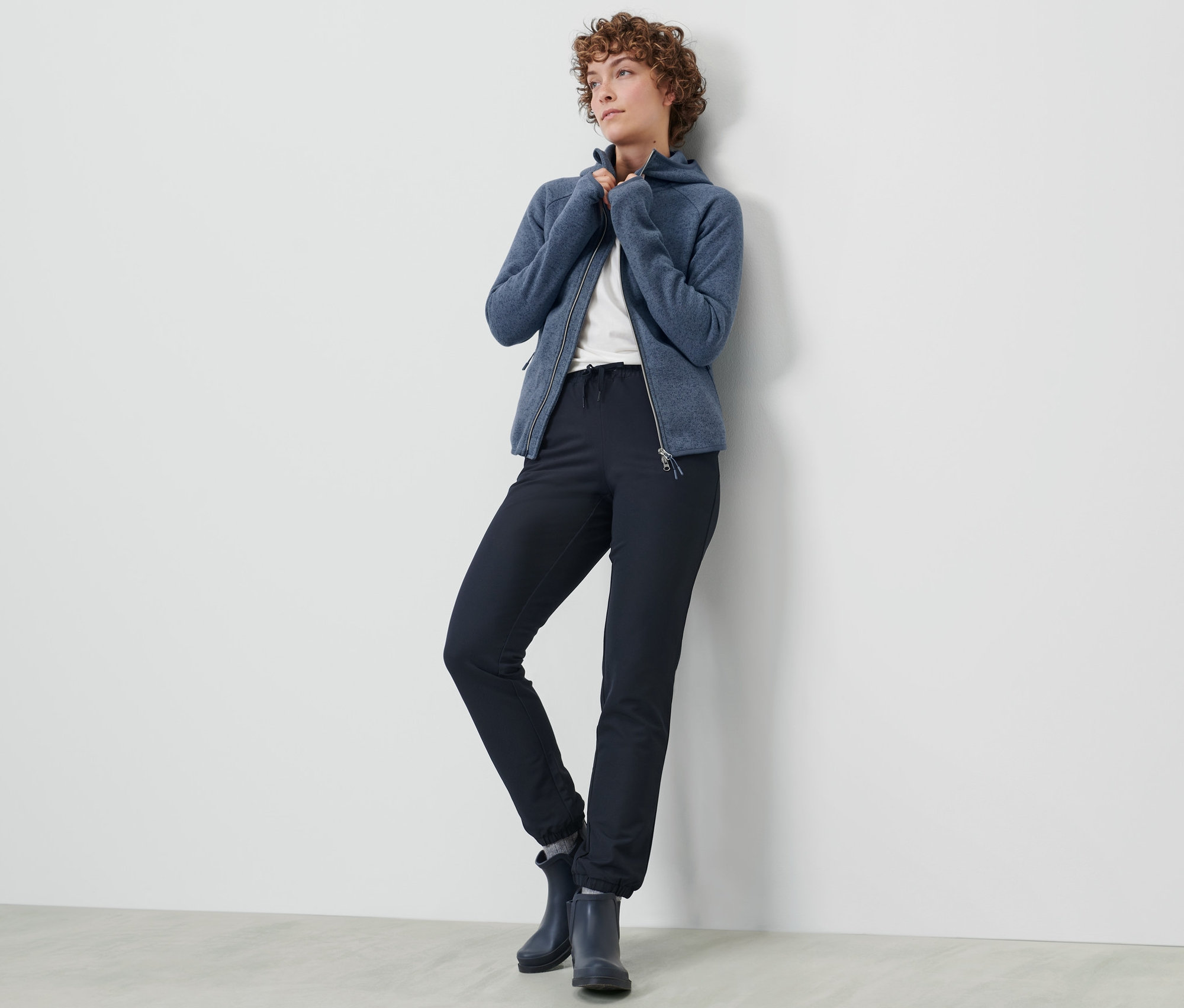 Žena pózuje v softshellových běžeckých kalhotách a modré mikině na zip.