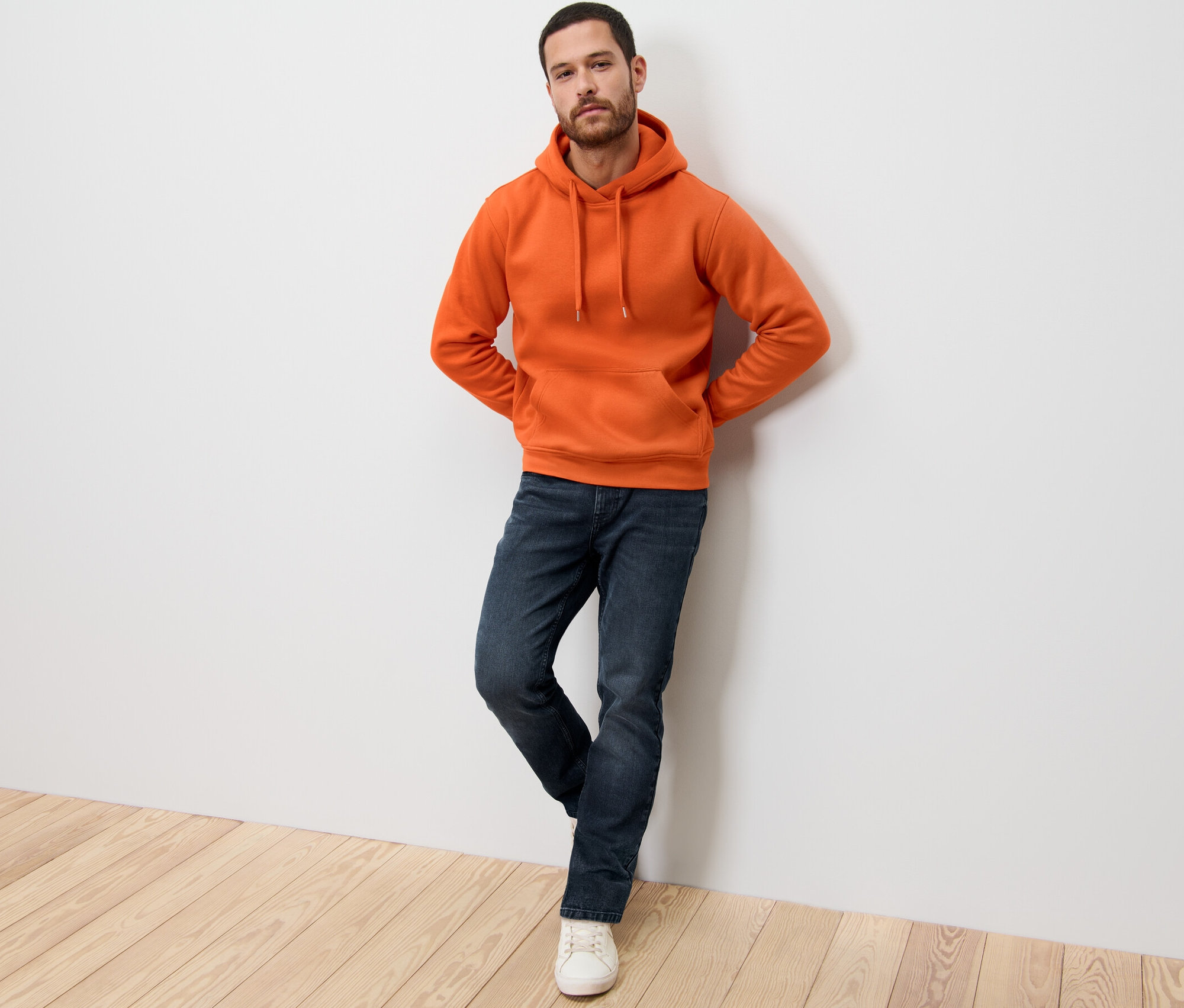 Muž opřený o zeď má na sobě oranžovou mikinu s kapucí.