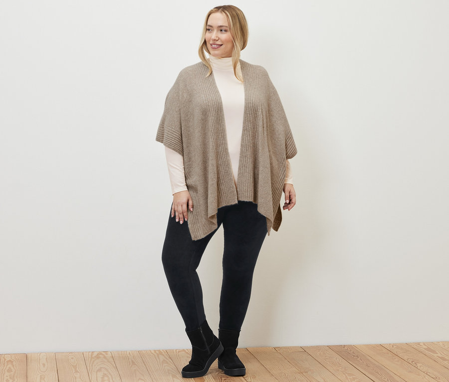 Žena má na sobě pletenou pelerínu, manšestrové legíny a krémově bílé triko s rolákem.