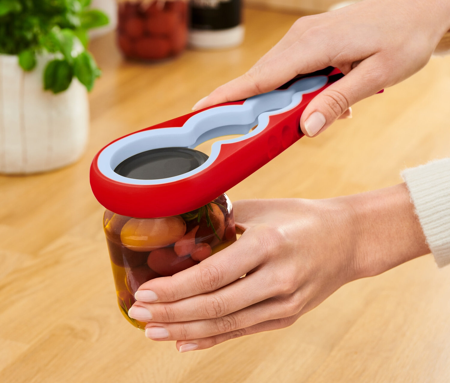 Žena otevírá sklenici s červeným otvírákem na sklenice a láhve.