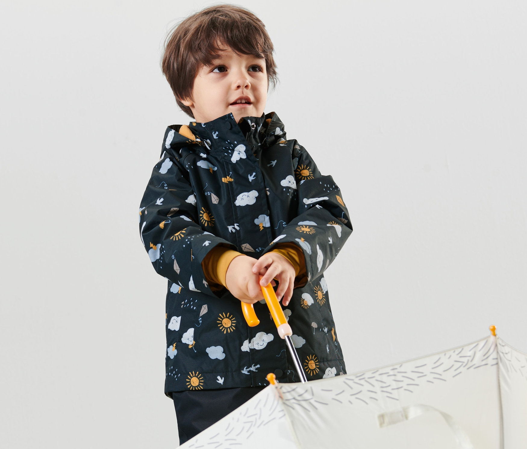 Chlapec drží bílý deštník a má na sobě tmavě modrou dětskou termo bundu do deště s celoplošným potiskem.
