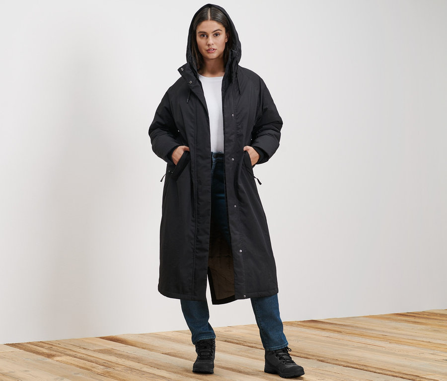 Žena stojí a má na sobě extra dlouhý termokabát a džíny Slim Fit Emma tmavě modré barvy.