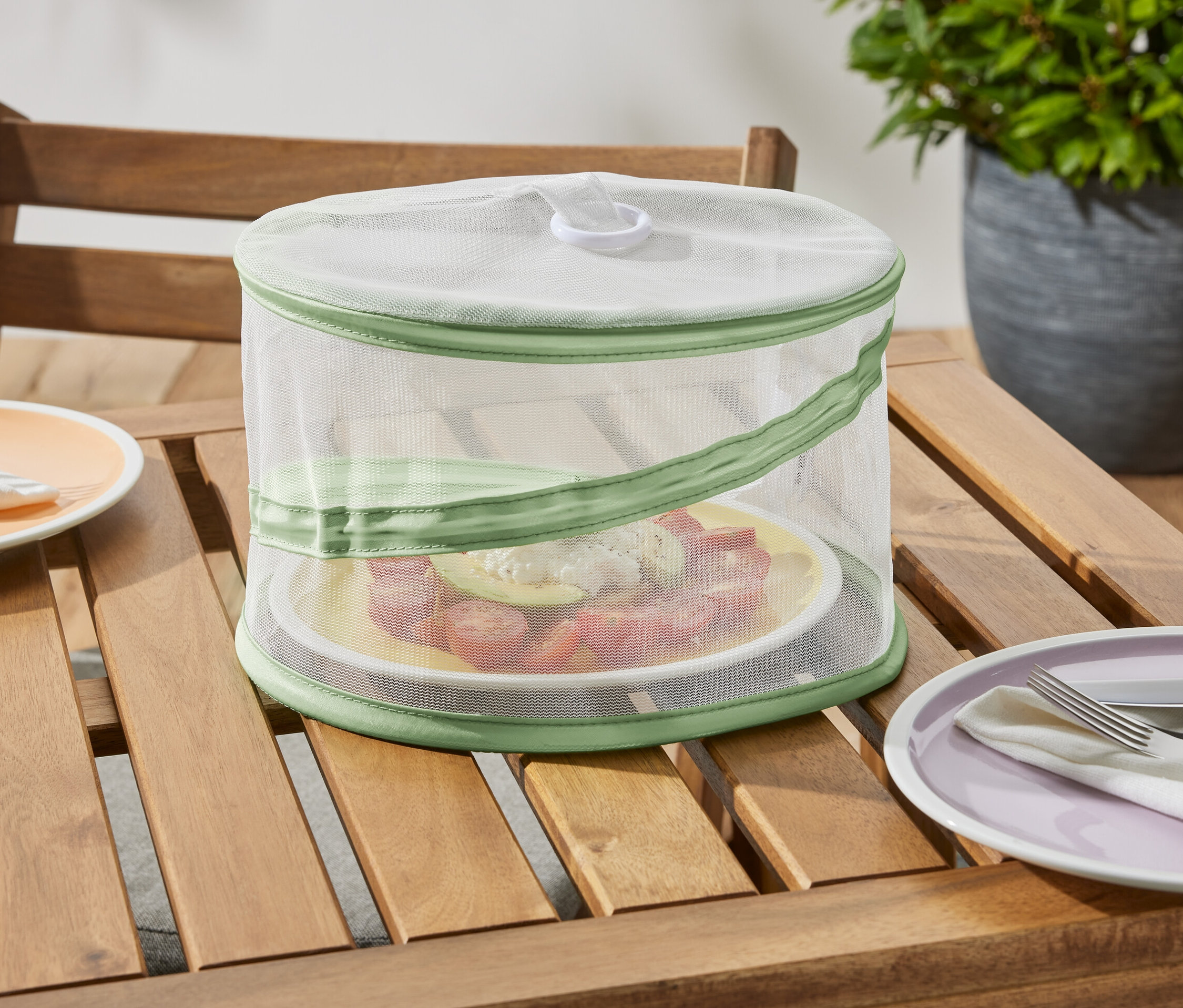 Skládací miniaturní kryt na jídlo stojí na dřevěném stole a chrání talíř s jídlem.