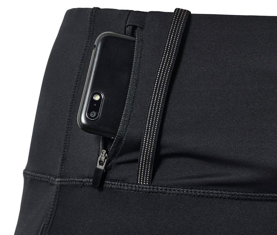 Detail černých běžeckých legín Performance s kapsou na zip, ve které je zasunutý mobilní telefon.