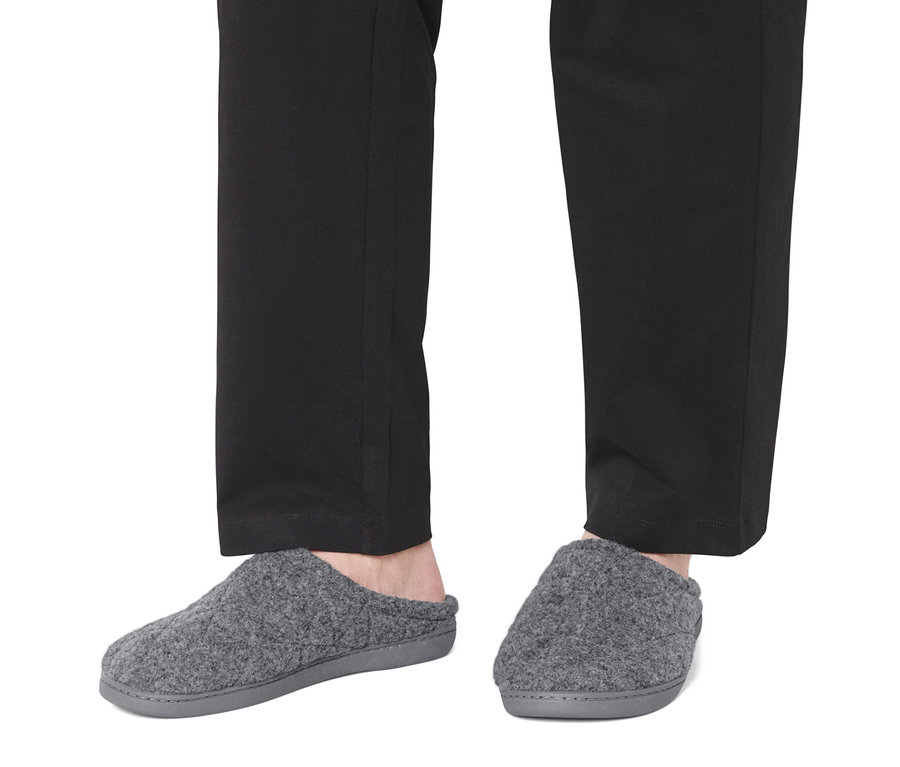 Nohy v černých kalhotách a šedých pantoflích.