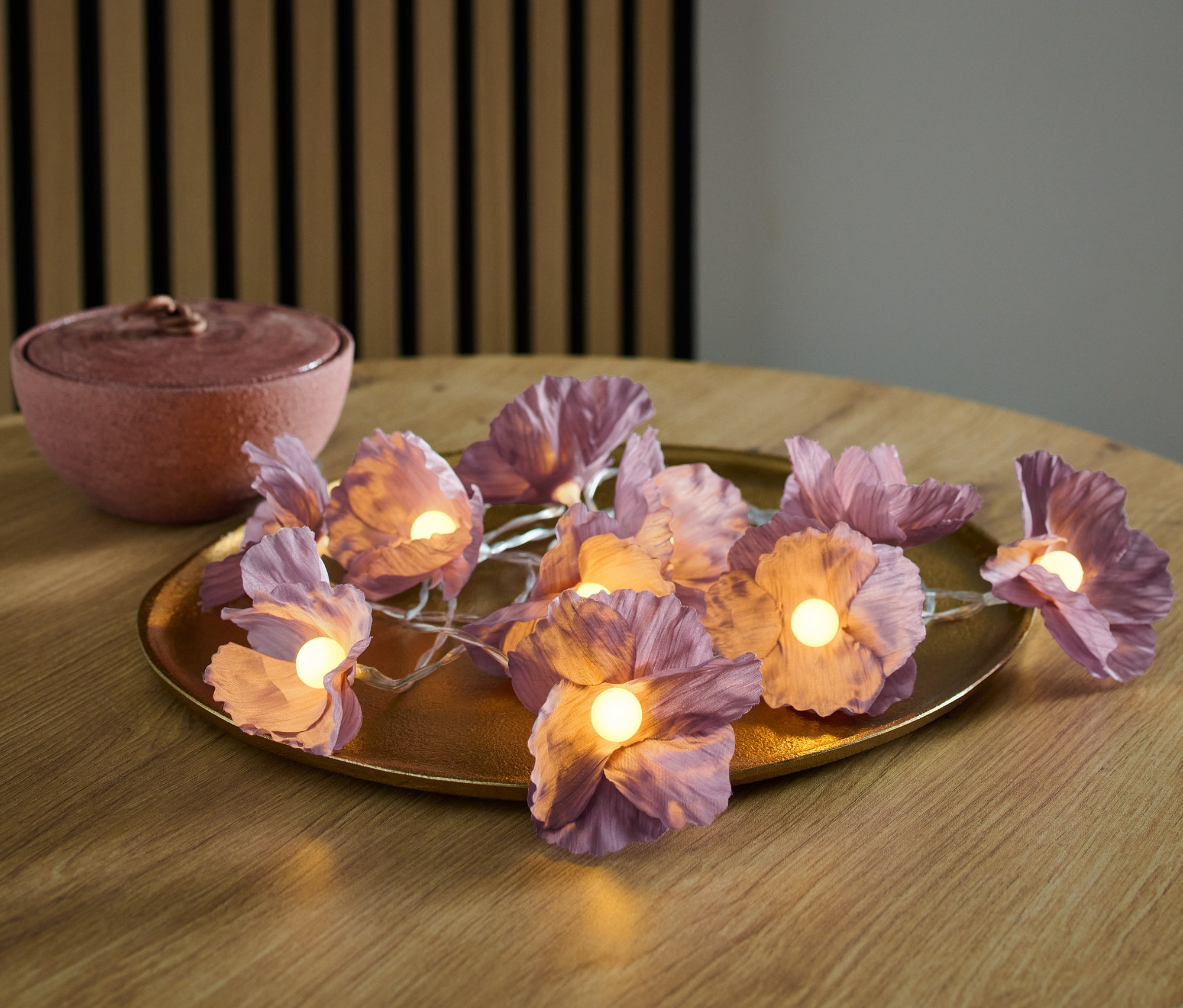 Květinový LED světelný řetěz na zlatém podnosu na dřevěném stole.