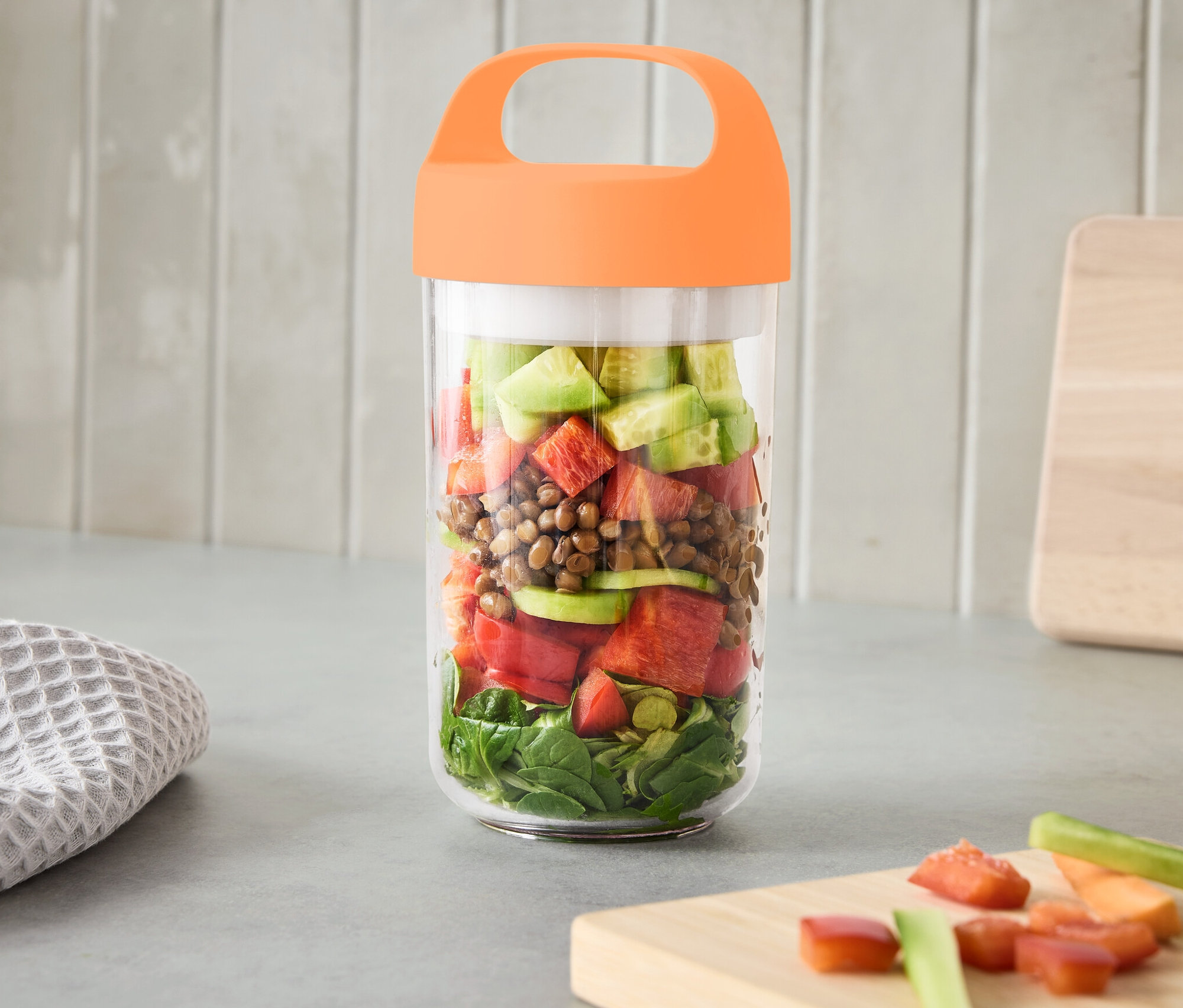 Cestovní nádoba s uchem, velká, plná zeleniny, stojí na lince.